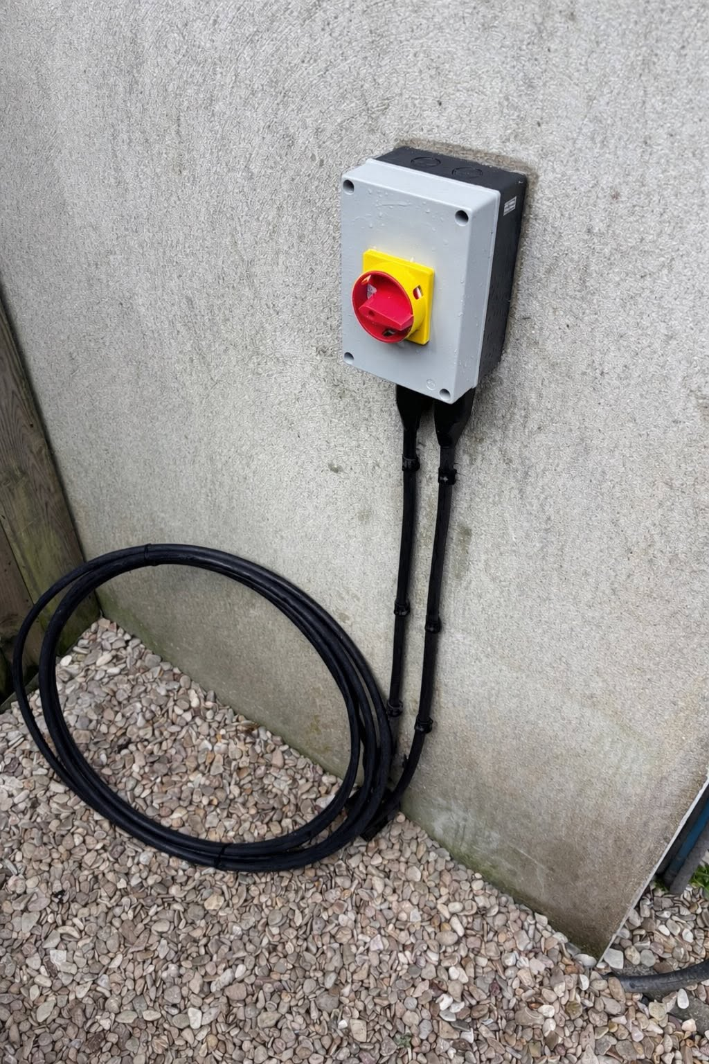 Weatherproof outdoor electrical enclosure with rotary isolator switch and cabling on an exterior wall