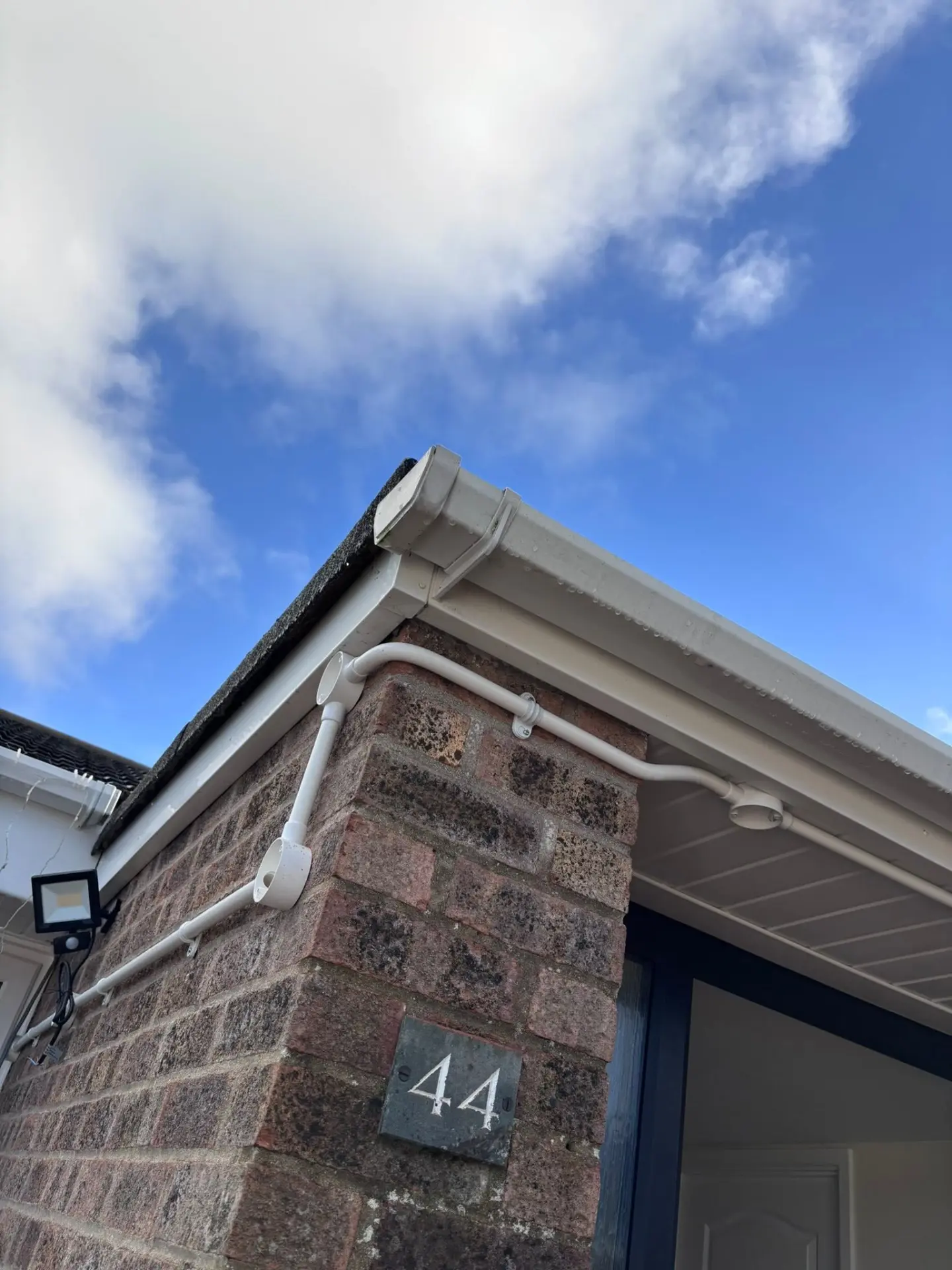 White conduit and cabling neatly routed around the exterior corner of a brick house with a security light